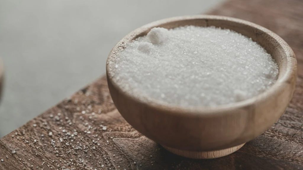 Wooden bowl filled with coarse salt crystals on a rustic wooden surface